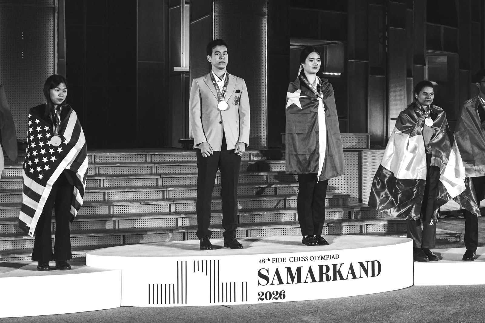 Individual medalists stand on the podium at the closing ceremony, some wrapped in national flags, in front of the Samarkand 2026 sign.